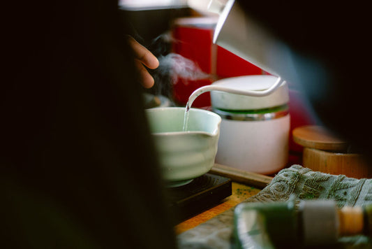 Hands pouring hot water over ceremonial grade matcha powder in a white bowl