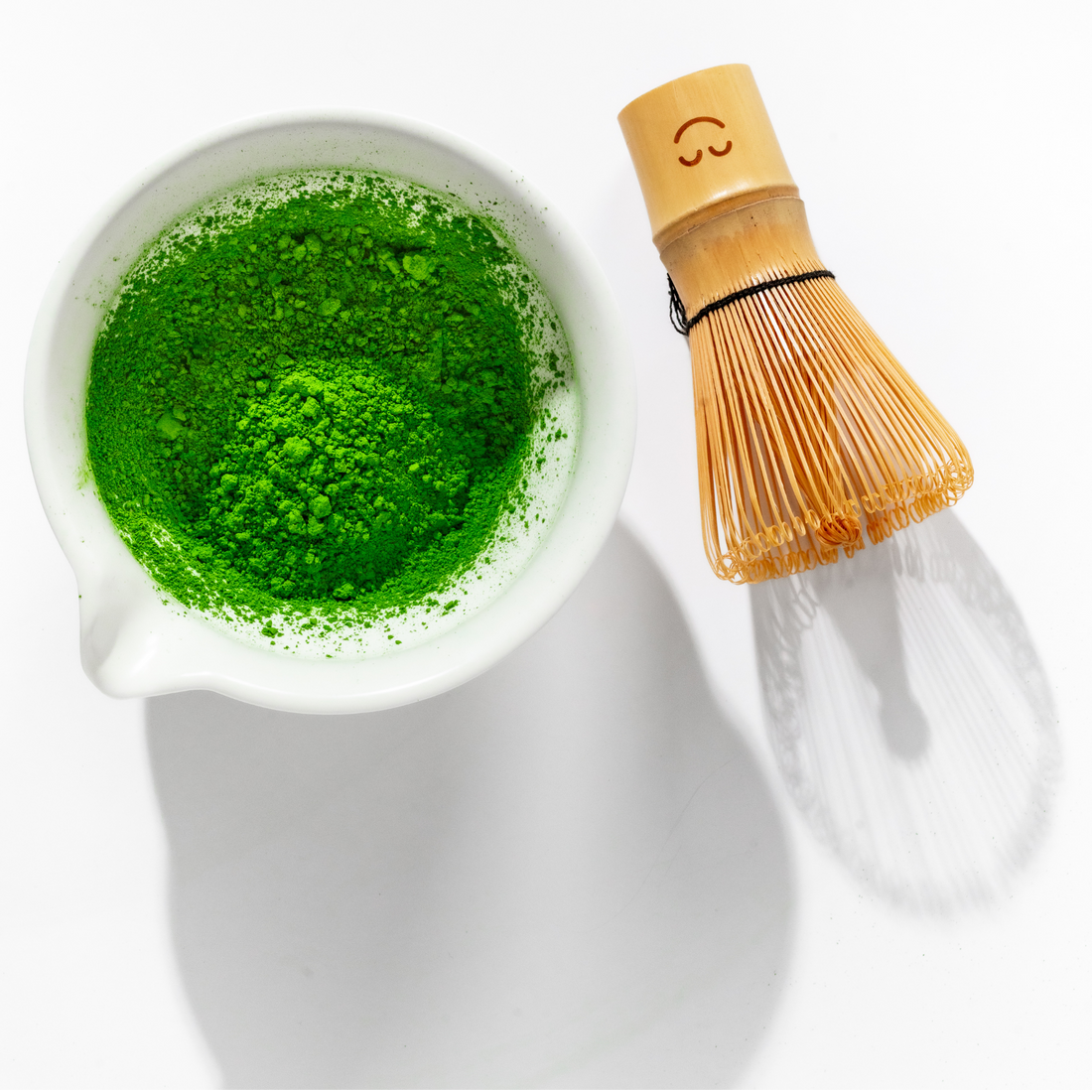 Bright green ceremonial grade matcha powder in a white bowl with a bamboo whisk